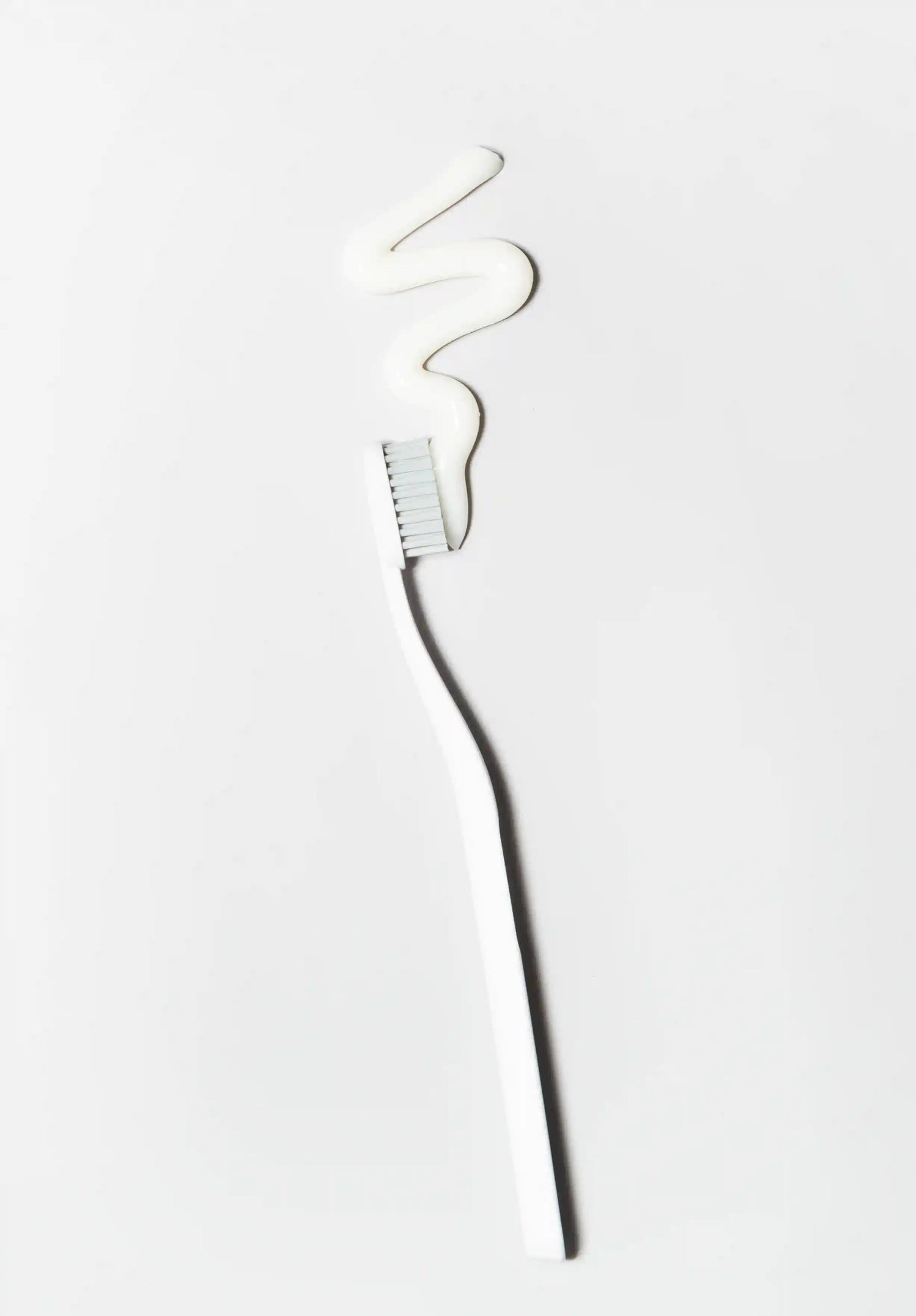 White toothbrush with a swoesh of white toothpaste on a white background